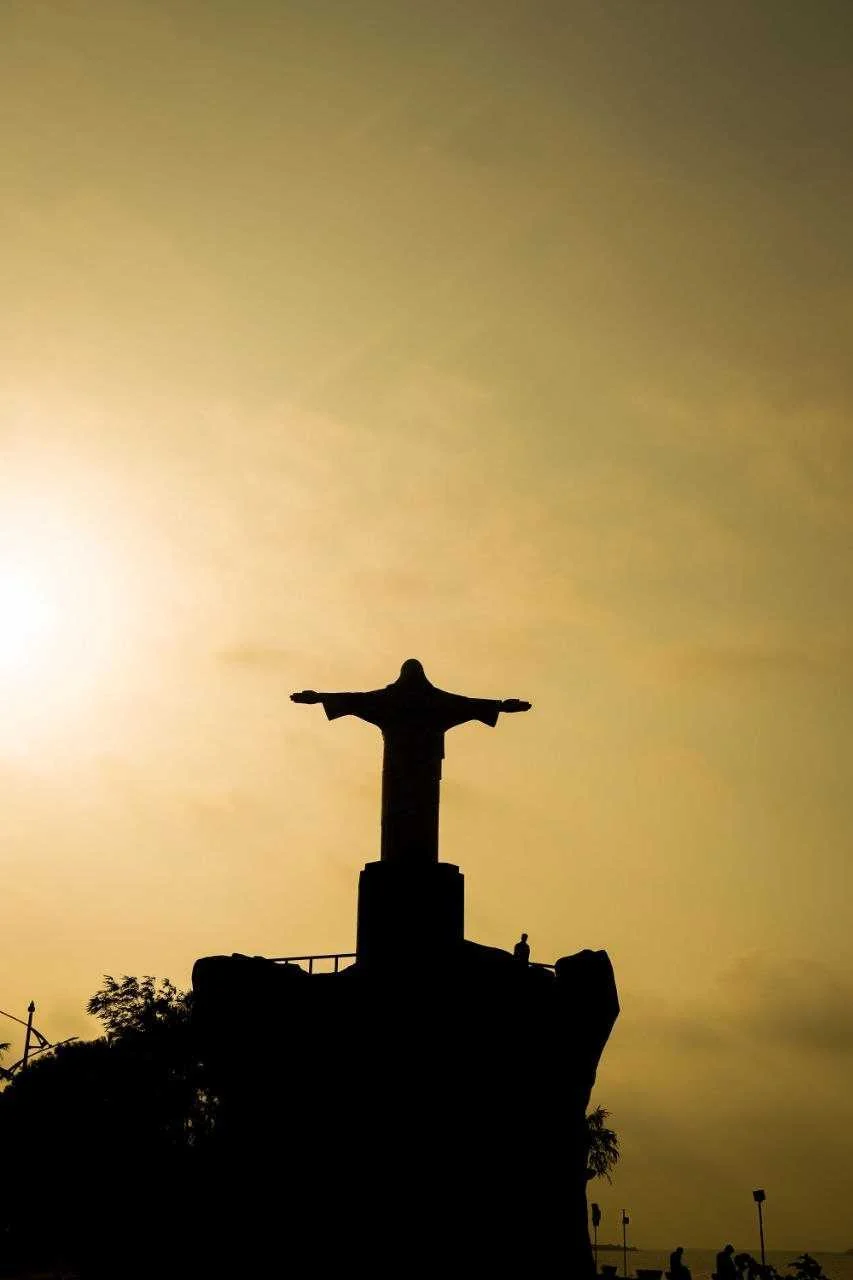 Silhouette of a figure with outstretched arms on a hill at sunset